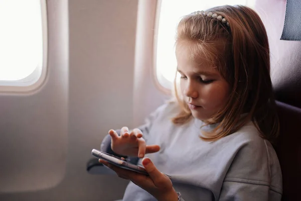 En liten flicka spelar spel på smartphone i ett flygplan säte — Stockfoto