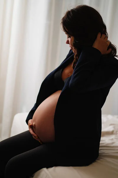 Una donna incinta in giacca nera con seni nudi e pancia sul letto — Foto Stock