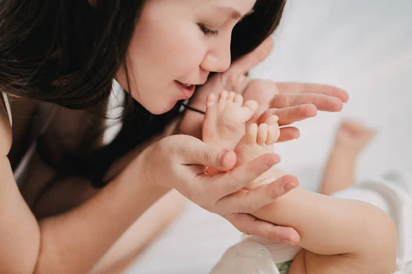 Una madre gentil y cariñosa besa las piernas del bebé. — Foto de Stock