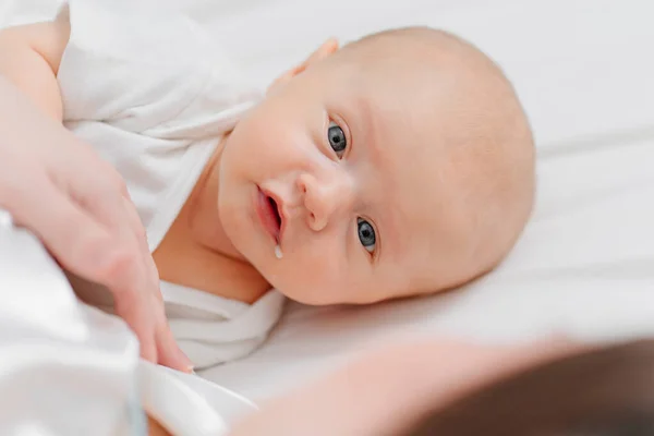 En söt baby med en droppe mjölk i hörnet av munnen på sängen nära mor. — Stockfoto