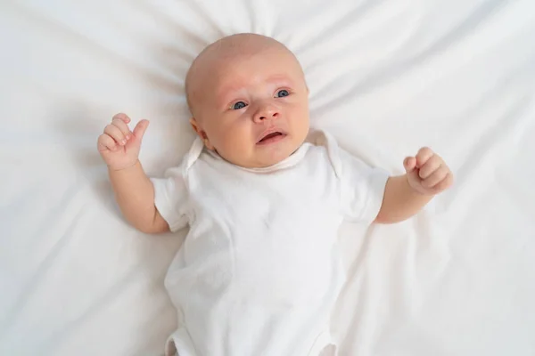 Um bebê recém-nascido chora em uma folha branca. birras infantis. vista superior. — Fotografia de Stock