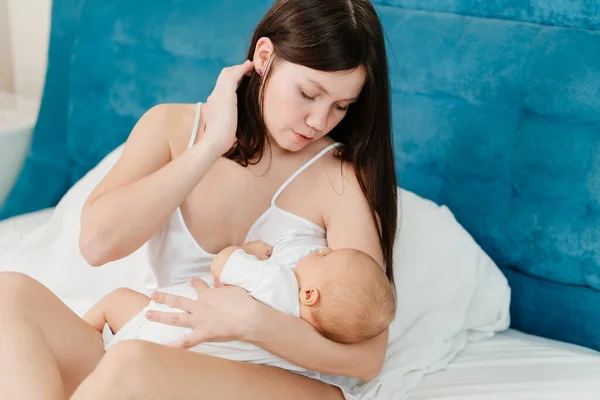 Alăptarea. mama în cămașă de mătase ține în brațe copilul în pat. — Fotografie, imagine de stoc