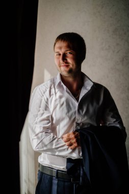 Beyaz gömlekli bir adam pencerede duran bir ceket tutuyor.