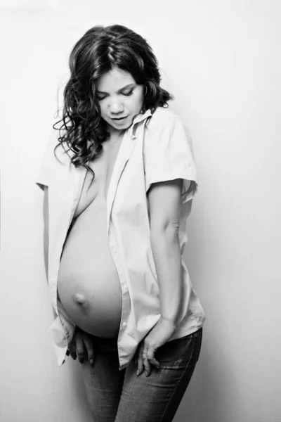 Attractive pregnant woman in jeans and a shirt on a naked body. womens health — Stockfoto