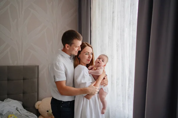 Una familia feliz con un bebé recién nacido junto a la ventana. mamá, papá y bebé. — Foto de Stock
