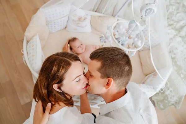 Vista desde arriba. padres a un bebé se encuentra en una cuna blanca con móvil con juguetes. —  Fotos de Stock