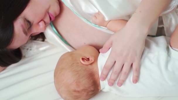 Amamantando. madre en un albornoz alimenta al bebé con leche materna acostada en la cama — Vídeos de Stock