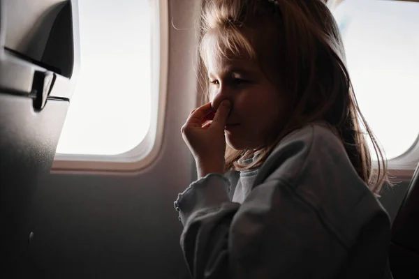 Una niña aprieta la nariz debido al olor desagradable en el asiento del avión por la ventana — Foto de Stock