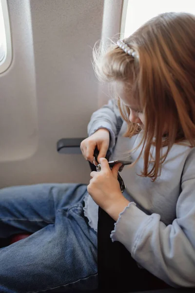 En liten flicka spänner fast säkerhetsbältet i en sittplats ombord på planet. — Stockfoto