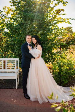 Gelin ve damat parkta yeşil yapraklı bir çalılığın yanında dururlar.. 