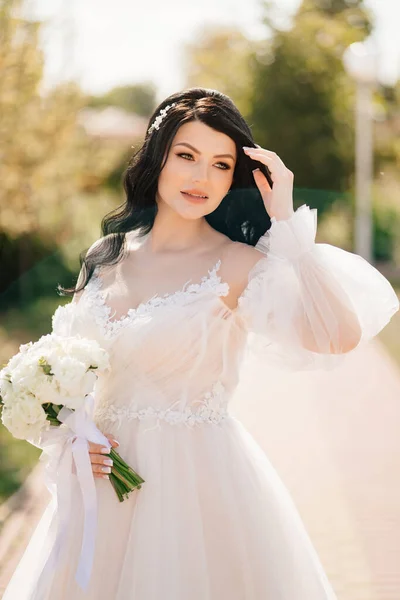Noiva morena em um vestido com um buquê de flores ao ar livre — Fotografia de Stock