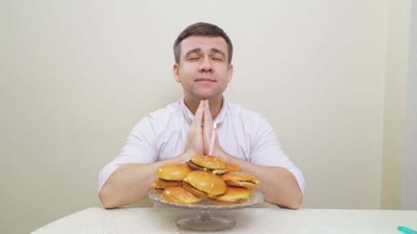 Hombre feliz pide deseo y sopla vela en pastel de hamburguesa. pastel para hombres. — Vídeos de Stock