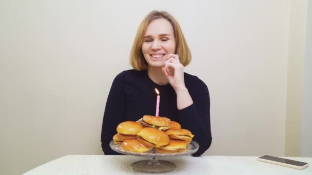 Una mujer pide un deseo y sopla una vela en un pastel de hamburguesas. pastel original. — Vídeos de Stock