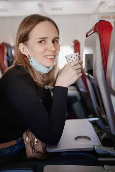 Una mujer con una máscara protectora bebe una bebida de una taza de papel a bordo del avión. — Foto de Stock