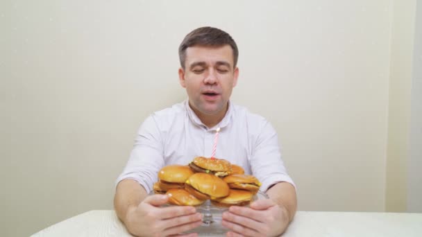 Een man doet een wens en blaast een kaars uit op een hamburgertaart. cake voor mannen. — Stockvideo
