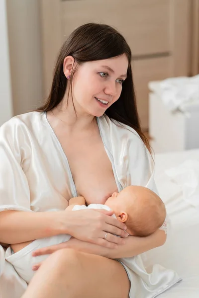 Amamantando. la madre en un albornoz alimenta al bebé con leche materna en la cama. —  Fotos de Stock