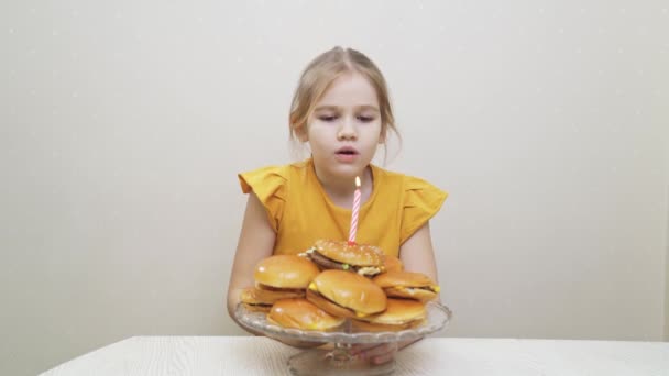 Vtipná holčička si něco přeje a sfoukne svíčku na hamburgerovém dortu. — Stock video