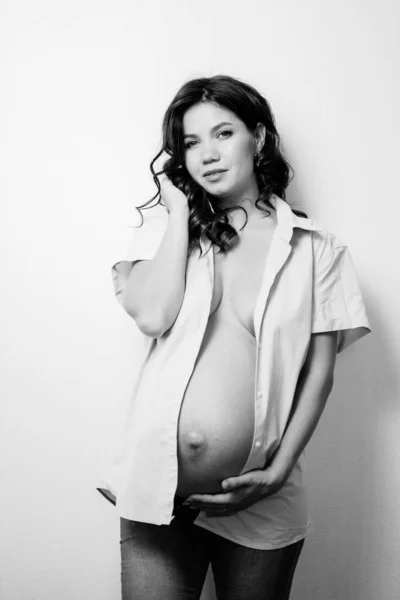 Attractive pregnant woman in jeans and a shirt on a naked body. womens health — Stockfoto