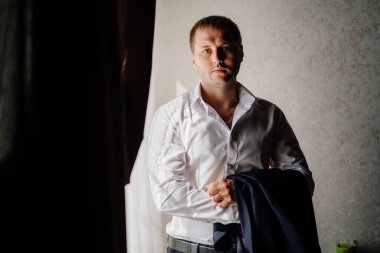 Beyaz gömlekli bir adam pencerede duran bir ceket tutuyor.