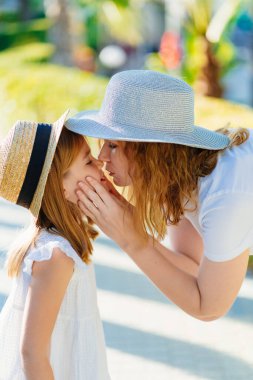 Anne ve kızı otelin tropikal parkında şapka takıyor.
