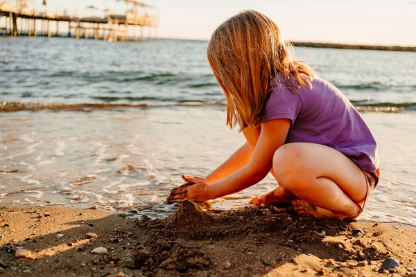 Симпатичная маленькая девочка сидит на берегу моря, играя в песке и с булыжниками. — стоковое фото