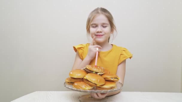 웃긴 작은 소녀가 소원을 빌고 햄버거 케이크에 촛불을 불어 넣습니다.. — 비디오
