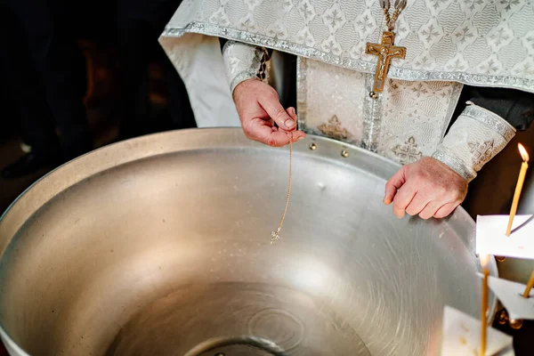 Ett kors på en guldkedja doppas i vatten för dop i kyrkans teckensnitt. — Stockfoto