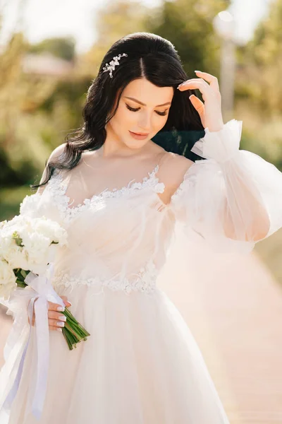 Noiva morena em um vestido com um buquê de flores ao ar livre — Fotografia de Stock