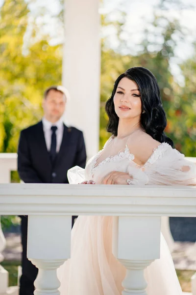 Panna młoda i pan młody w sukniach ślubnych na balustradzie w altanie lub rotundzie w parku. — Zdjęcie stockowe