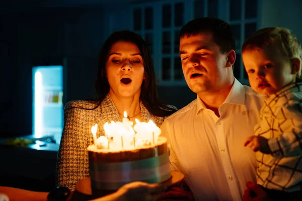 Um pai e uma mãe com um filho criança fazem um desejo e apagam velas no bolo. — Fotografia de Stock