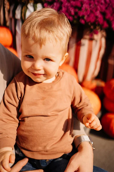 Um menino loiro bonito em uma camisola marrom nos braços dos pais. — Fotografia de Stock