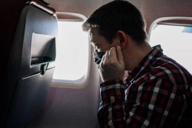 Adam uçaktaki pencerenin yanındaki siyah koruyucu maskeyi ve ekose gömleği düzeltiyor..