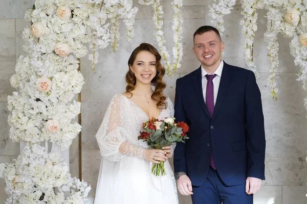 Красива і щаслива наречена і наречена в арці квітів на весільній церемонії — стокове фото