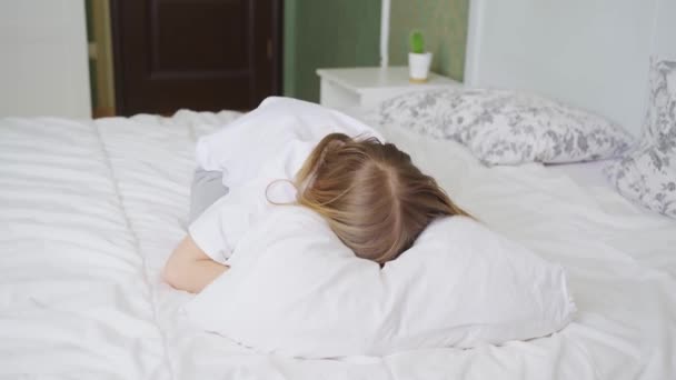 Una niña en una cama en el dormitorio y llora con la cara enterrada en la almohada — Vídeo de stock