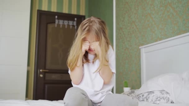 Una niña pequeña se sienta en una cama en el dormitorio y llora. — Vídeo de stock
