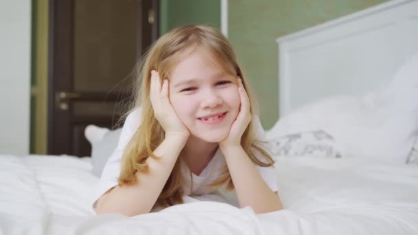 Una linda niña se encuentra en la cama en casa. — Vídeo de stock