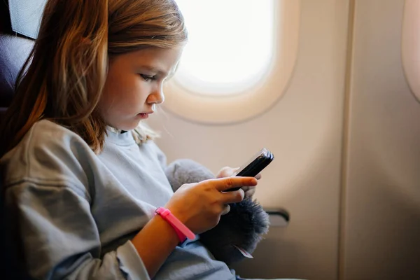 En liten flicka spelar spel på smartphone i ett flygplan säte — Stockfoto