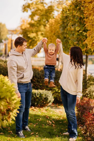 Uma família feliz segurando as mãos de um jovem filho uma caminhada de outono. — Fotografia de Stock