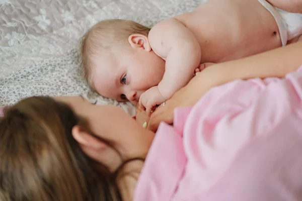 Mamá yace en la cama con el bebé. la felicidad de la maternidad. lactancia materna. — Foto de Stock