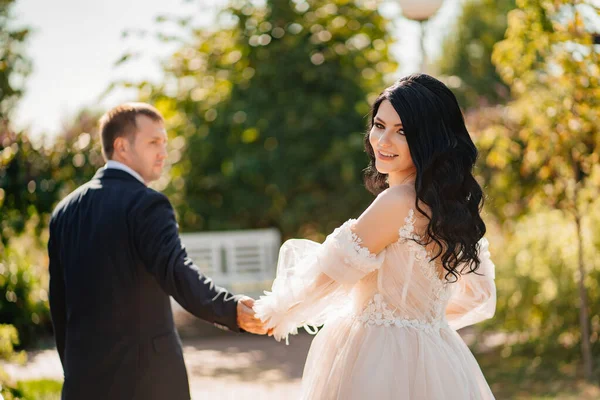 Bride and groom walk holding hands through park. wedding walk. view from back — Stockfoto