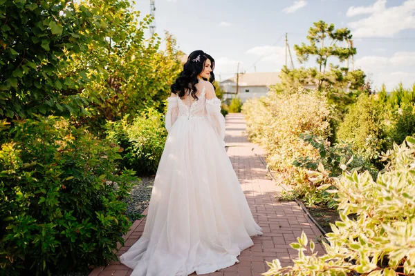 Blick von hinten. eine Braut geht im Hochzeitskleid den Weg im Park entlang. — Stockfoto