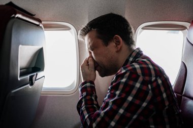 Ekose gömlekli bir adam cam kenarındaki koltukta burnunu siliyor.. 