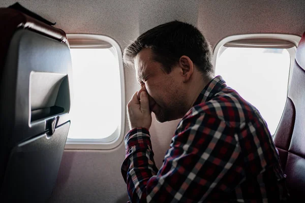 격자무늬 셔츠를 입은 한 남자가 창문 좌석에 있는 비행기에 코를 부는 모습. — 스톡 사진