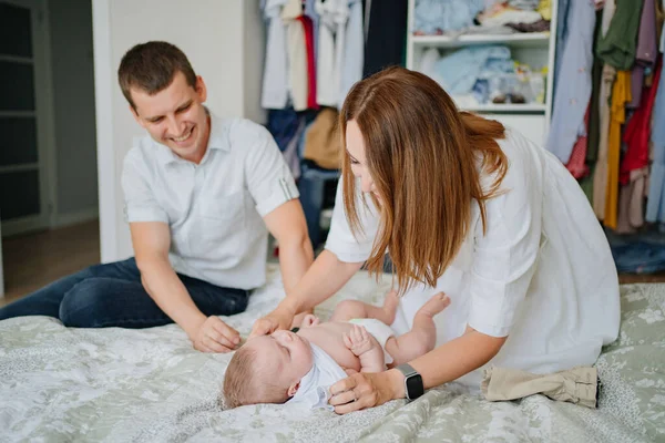 Padres cambiándose de ropa un bebé yace en una cama blanca —  Fotos de Stock