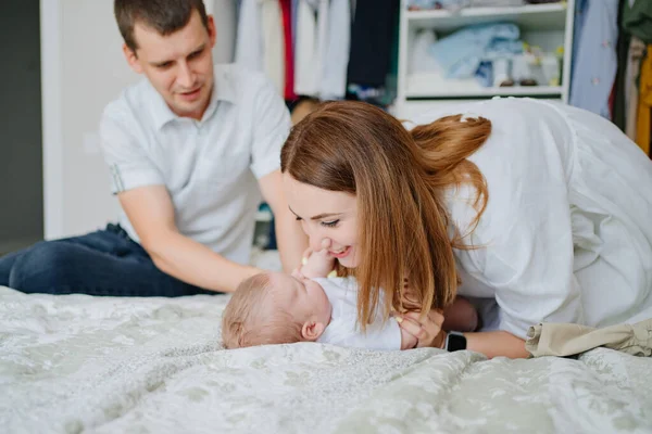 Padres cambiándose de ropa un bebé yace en una cama blanca —  Fotos de Stock