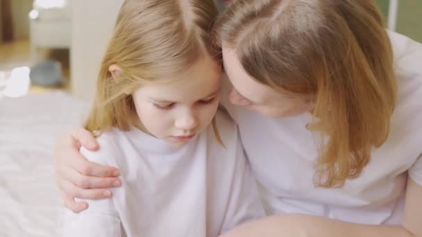 Mamá abraza y consuela a su pequeña hija molesta en casa. — Vídeo de stock