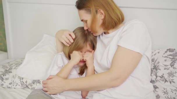 Мама обіймає і втішає свою засмучену маленьку доньку в спальні — стокове відео