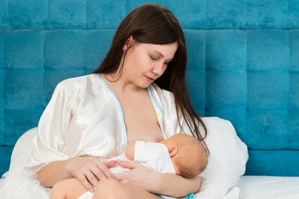 Alăptarea. mama într-o haină de mătase hrănește copilul cu lapte matern în pat. — Fotografie, imagine de stoc