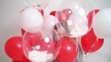 Sarışın bir kadın dans eder ve beyaz arka planda balonlarla eğlenir.. 