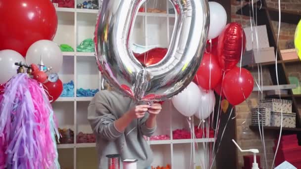 Una donna gonfia un palloncino a forma di grande numero d'argento per un compleanno — Video Stock